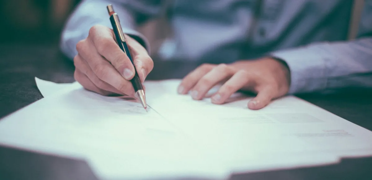 Persona revisando y firmando documentación sobre una mesa